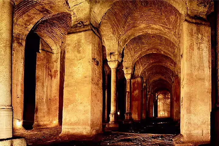Dimly lit Roman underground corridor with massive stone columns and vaulted ceilings on San Clemente Basilica private tour
