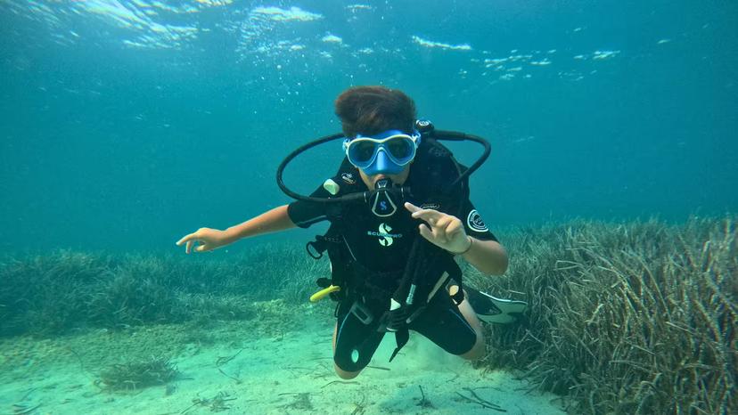 Young diver exploring underwater marine life during a baptism dive at Argentiera, Sassari, surrounded by aquatic plants.