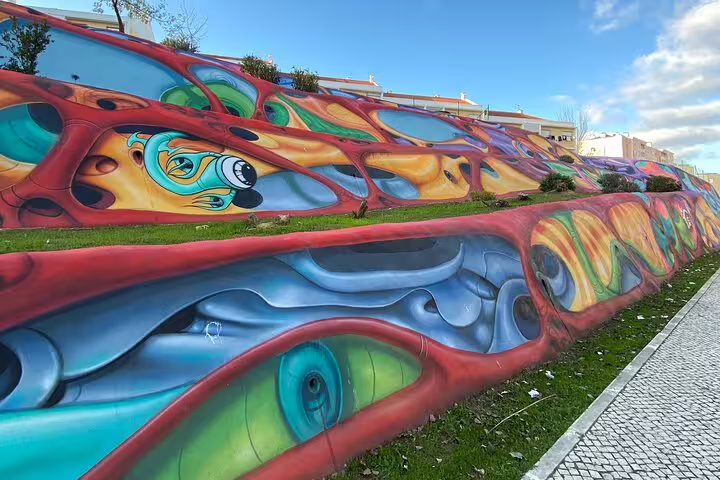 Dynamic urban mural with flowing abstract forms and vibrant colors on Lisbon hillside, celebrating street art.