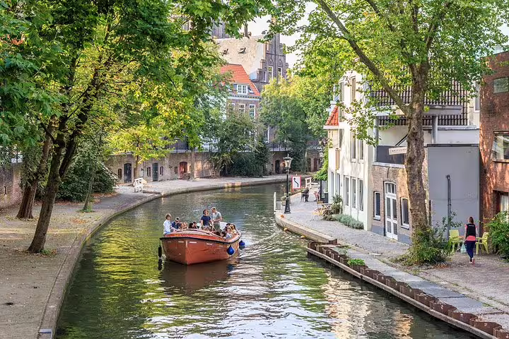 Boat cruising Utrecht canal by historic houses and trees, a scenic stop on a self-paced e-scavenger hunt