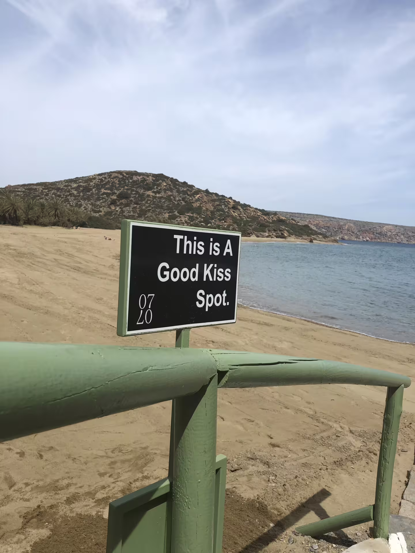 Romantic beachside view at Vai with a sign indicating 'This is a Good Kiss Spot', ideal for couples on tour.