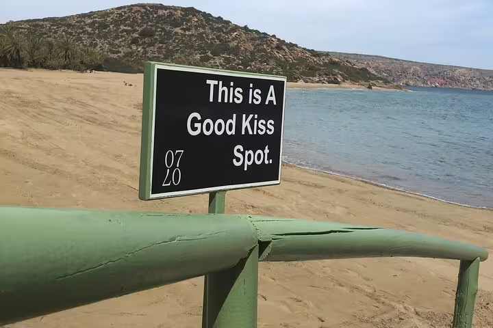 Discover the romantic charm of Vai's coastal landscape with a sign marking an ideal spot for a kiss.