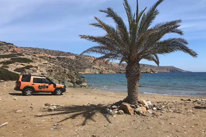 Explore the serene beachscape of Vai with a vibrant orange safari vehicle next to a solitary palm tree.