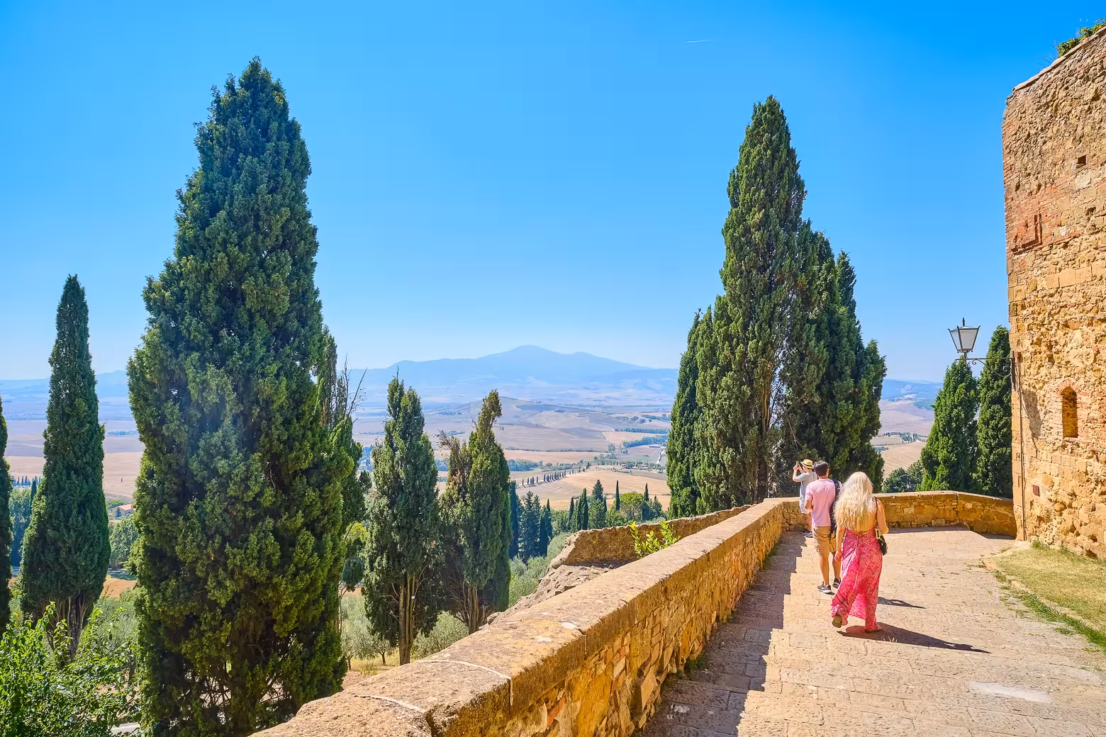 Visitors enjoy panoramic views of the Tuscan countryside and cypress trees on a walkway in Val d'Orcia.