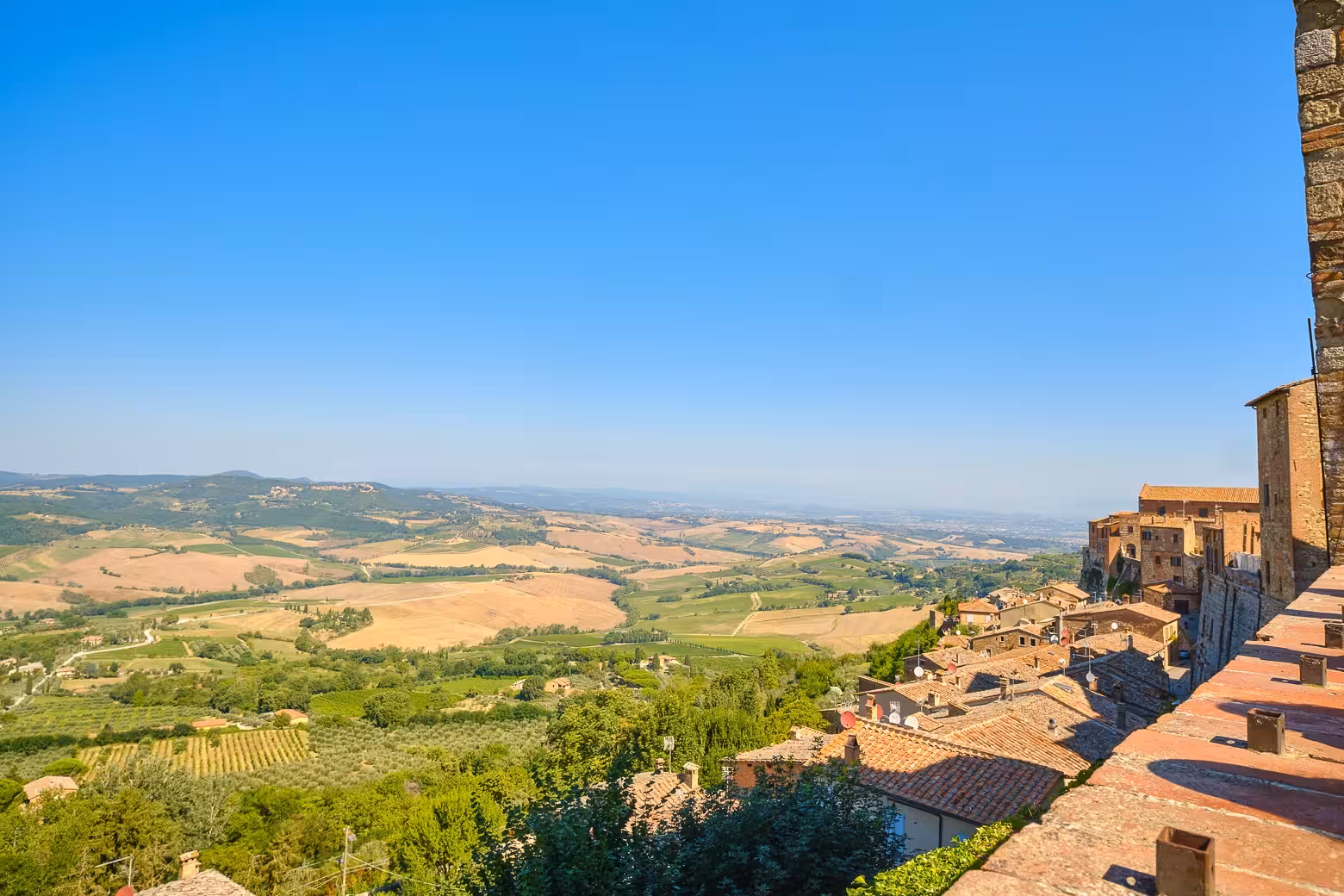 Panoramic view of Val D'Orcia's rolling hills and vineyards, showcasing the picturesque Tuscan landscape under a sunny sky.
