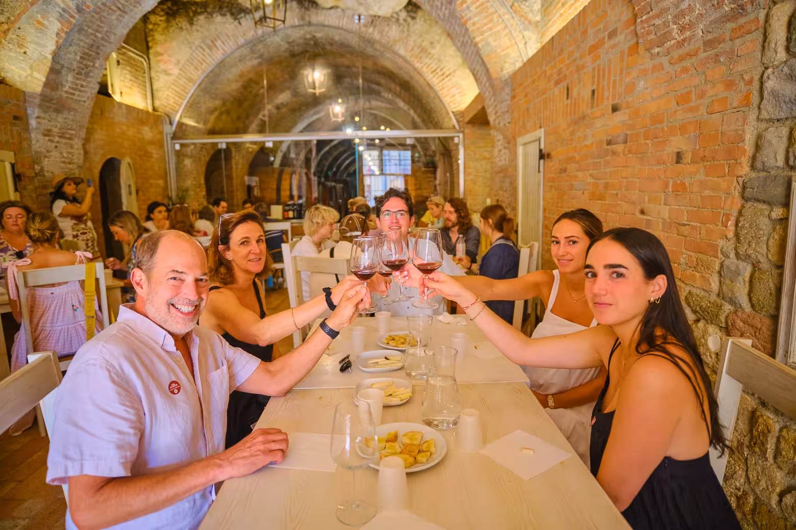 Group enjoying wine and cheese tasting in a rustic Val D'Orcia cellar on a full-day tour to Montalcino, Montepulciano, and Pienza.