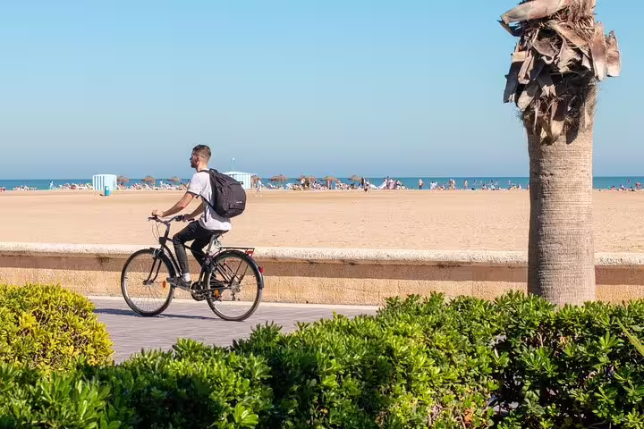 Cyclist enjoying a sunny day on Valencia beach promenade during a private bike and e-bike tour with scenic views and drinks.