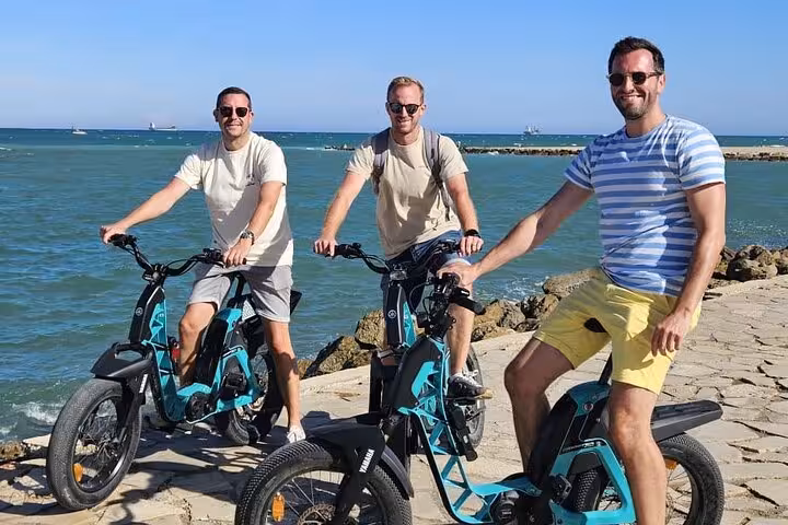 Friends on e-bikes riding Valencia seaside promenade, part of land and sea tour with catamaran cruise
