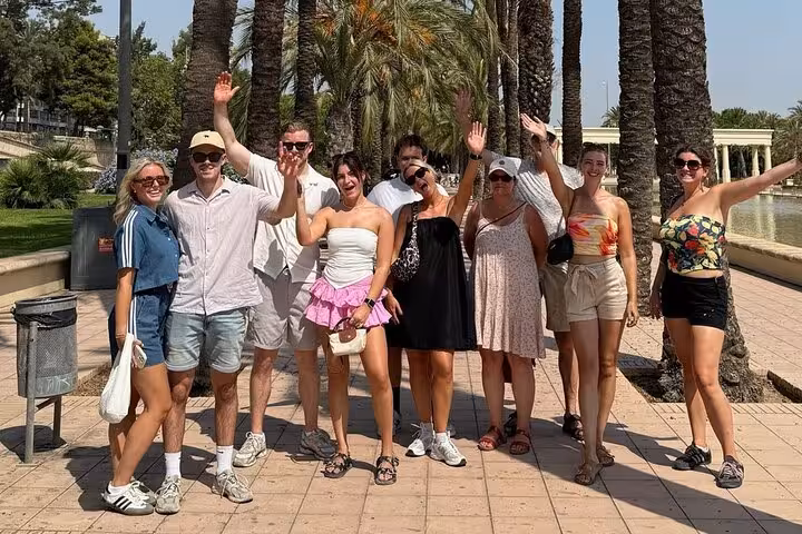 Friends on Valencia e-bike tour waving under palm trees near Turia Gardens, beaches, old town and arts route