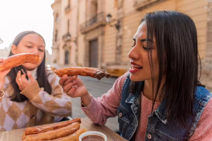 Family enjoying churros with chocolate on a charming street during a Valencia private tour, capturing authentic Spanish flavors.