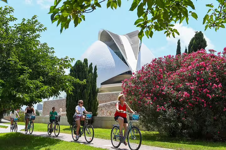 Cyclists enjoy a scenic Valencia private bike and e-bike tour with lush greenery and modern architecture in the backdrop.