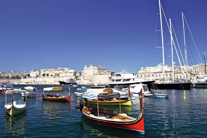 Colorful traditional boats and modern yachts in Valletta's bustling harbor against a backdrop of historic buildings.