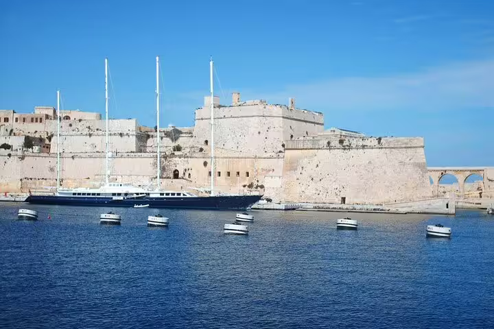 Elegant sailboats anchored near historic fortifications in Valletta's picturesque harbor under a clear blue sky.