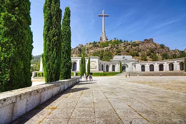 Visitors walking towards the grand Valley of the Fallen monument under a clear blue sky near Madrid.