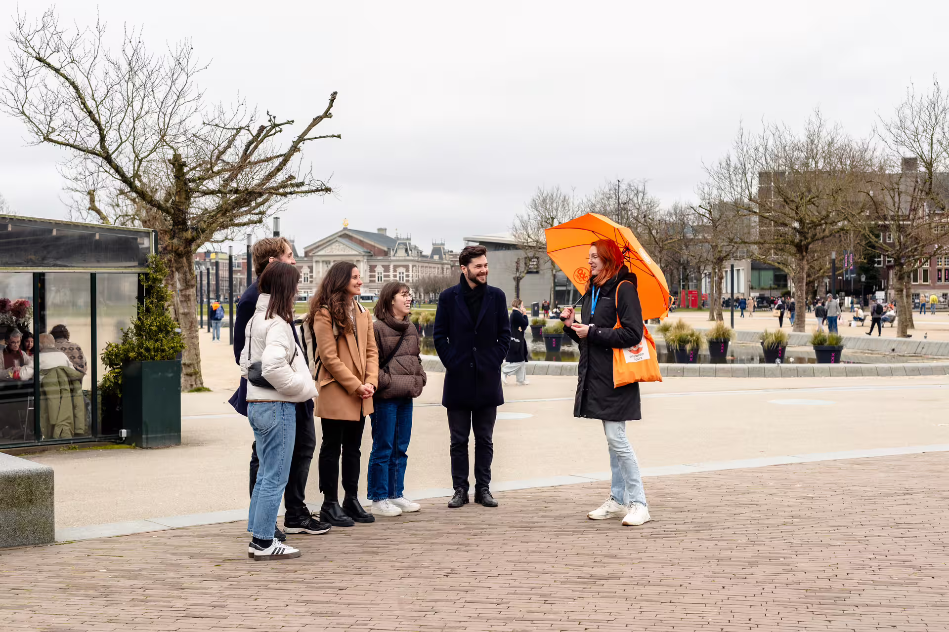Tour guide with orange umbrella leads group on Van Gogh Guided Tour in Amsterdam, exploring art history and local culture.