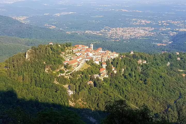 Aerial view of a picturesque hilltop village surrounded by lush forests near Varese, part of a customizable Milan to Varese tour.