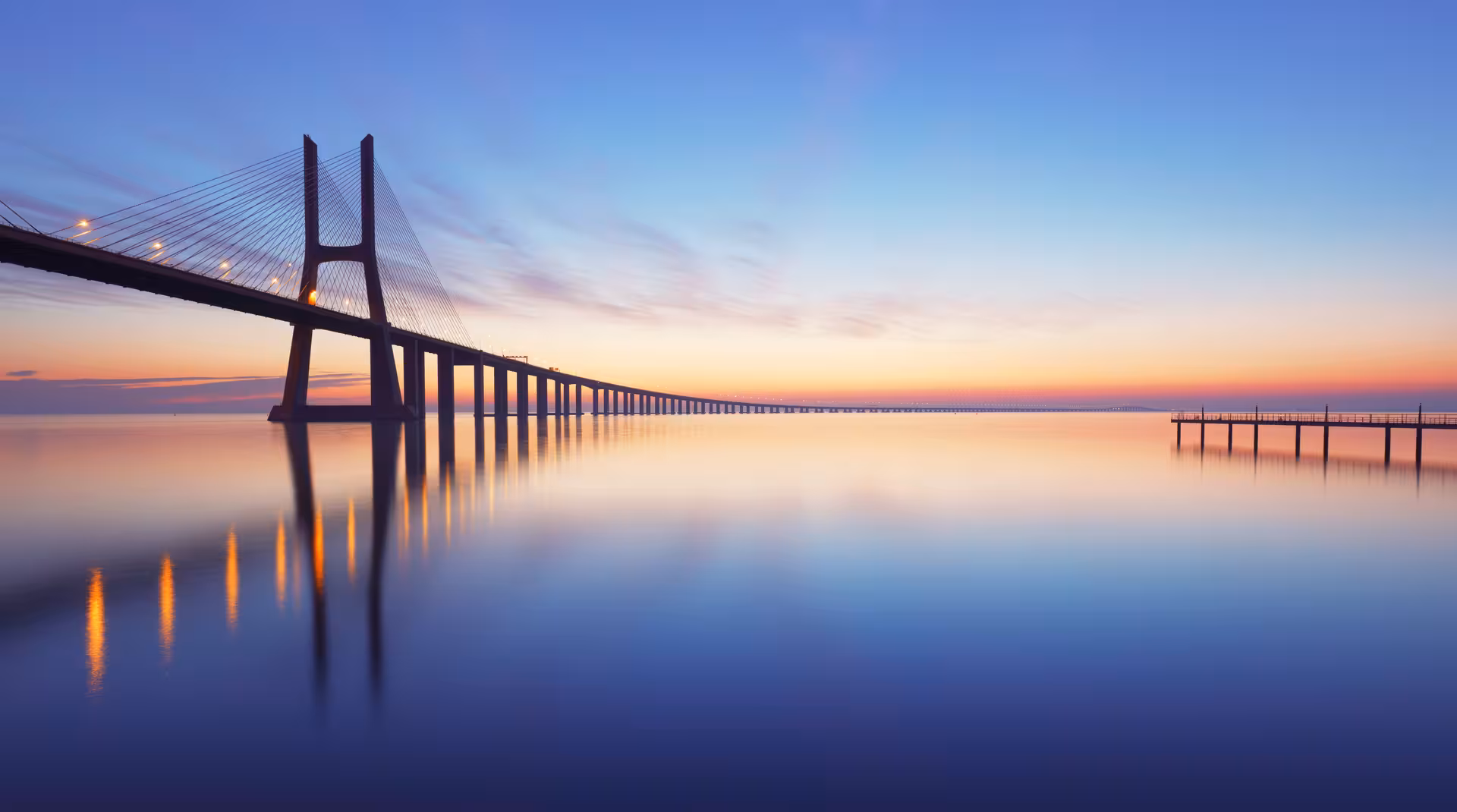 Panoramic view of the Vasco da Gama Bridge at sunrise over the calm waters of the Tagus River in Lisbon.