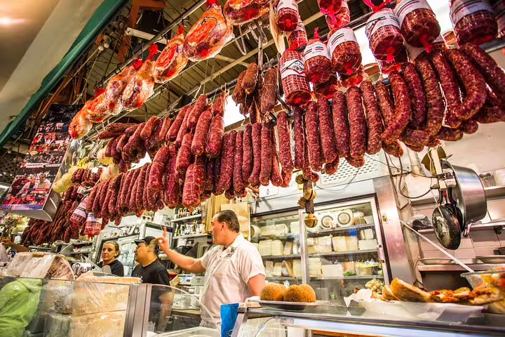 Vibrant market scene at The Vatican Market Experience showcasing a variety of hanging cured meats and local delicacies.
