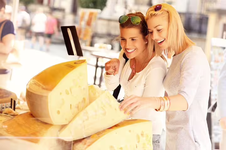 Two women enjoy selecting cheeses at an outdoor market stall during The Vatican Market Experience tasting and cooking class.