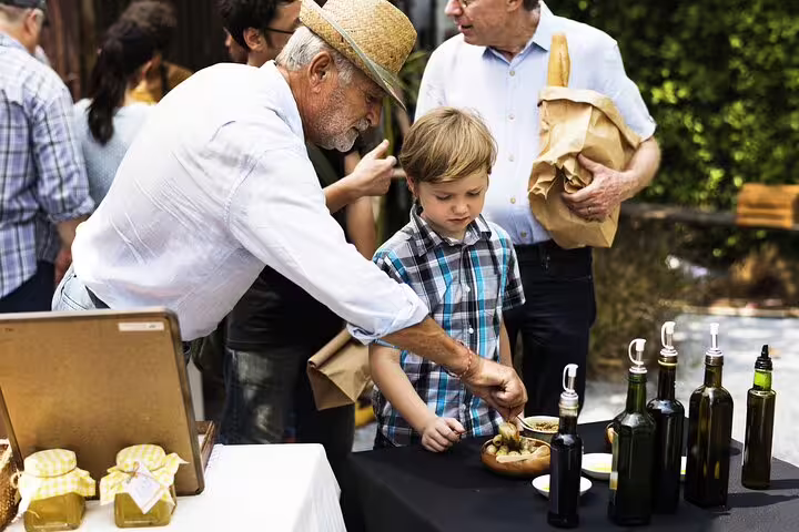 A man and child sample olive oils and bread at a vibrant outdoor market during the Vatican Market Experience tasting tour.