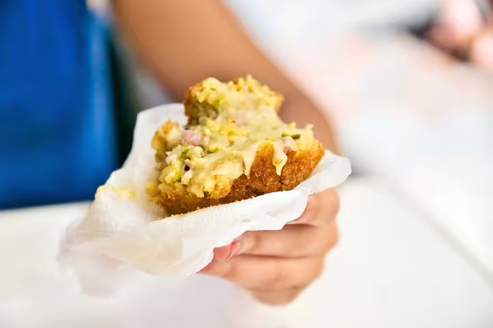 A hand holding a freshly made slice of pizza al taglio with toppings, part of The Vatican Market Experience cooking class.