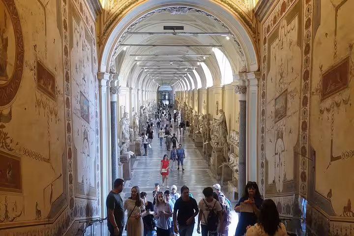 Tourists walk through the grand corridors filled with statues at the Vatican Museum, highlighting a guided tour.