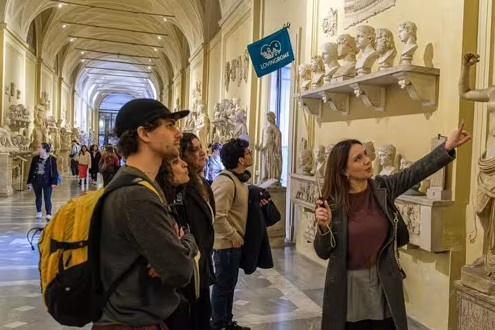 Tour group explores Vatican Museum's sculpture gallery with a guide highlighting art pieces.