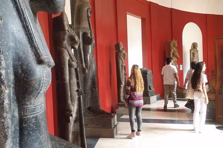 Visitors admire ancient sculptures in the Vatican Museum's vibrant red-walled gallery on a guided tour.