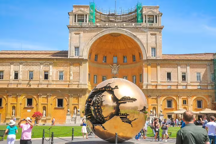 Visitors explore the Vatican Museums courtyard in Rome, admiring the bronze Sphere Within Sphere sculpture on a sunny tour day