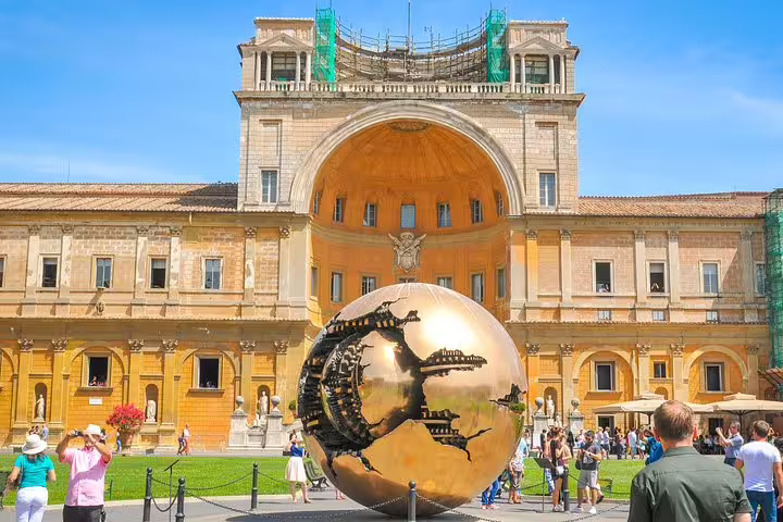 Tourists exploring the Vatican Museums courtyard with the golden Sphere Within Sphere sculpture on a guided Sistine Chapel tour