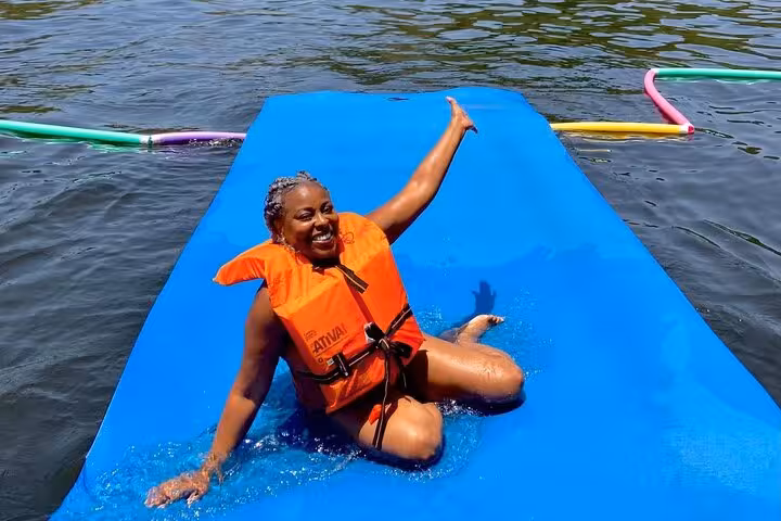 Guest in life vest lounging on floating mat during Velas do Rio private catamaran cruise with open bar
