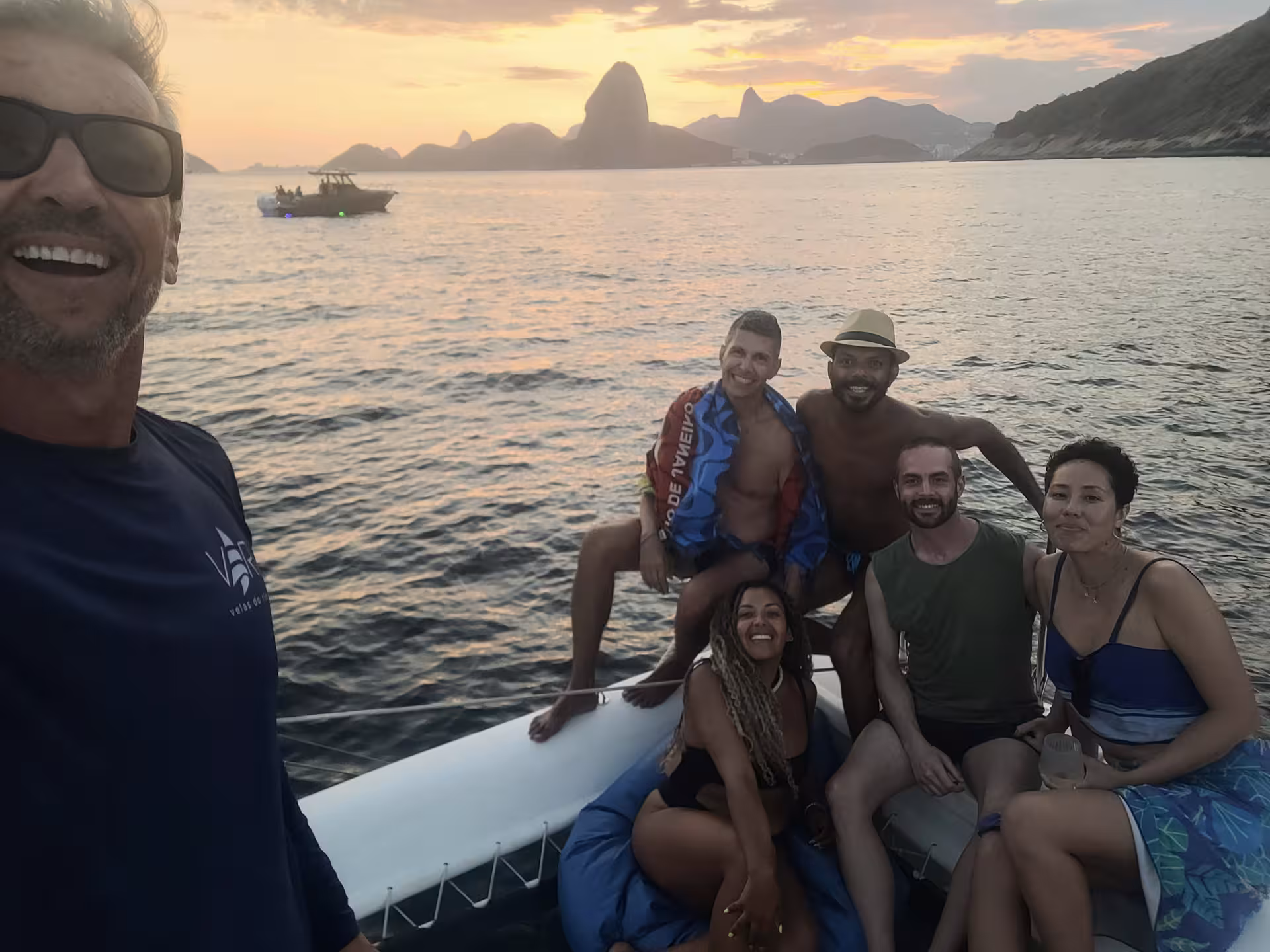 Group selfie on Velas do Rio shared catamaran at sunset in Guanabara Bay, Rio de Janeiro skyline