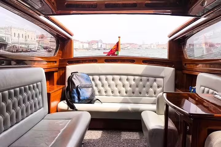 Luxurious interior of a Venetian boat showcasing plush seating and panoramic views of the Grand Canal.