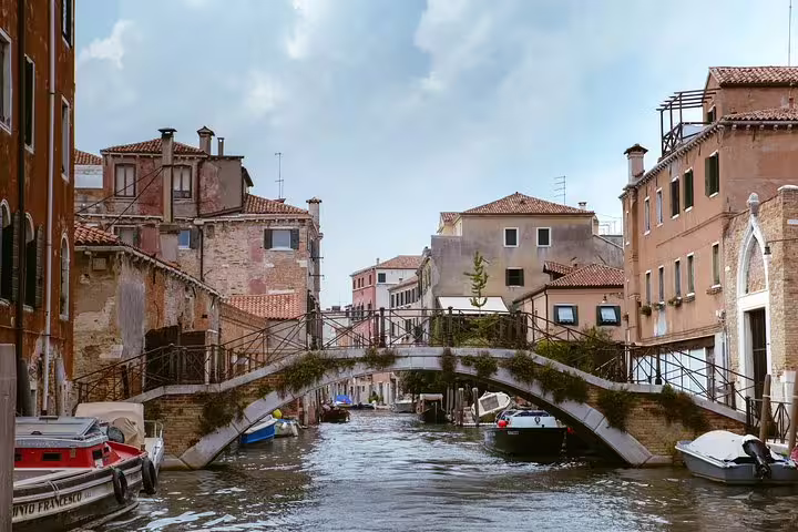 Charming Venetian canal with arched bridge and rustic buildings, a highlight of the Murano and Burano tour.