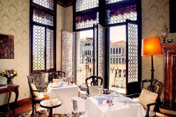 Elegant dining room with open windows overlooking Venetian architecture, perfect for a romantic dinner in a palace.