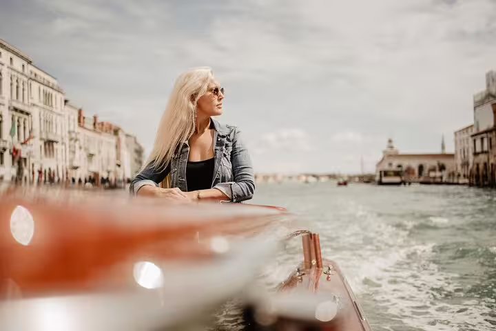Stylish woman on a Venetian water taxi tour with a professional photographer capturing iconic canal views.