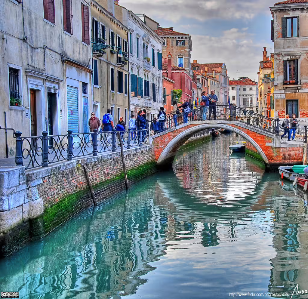Tourists cross a stone bridge over a quiet Venice canal, lined with colorful historic palazzi on a 2-day trip from Rome
