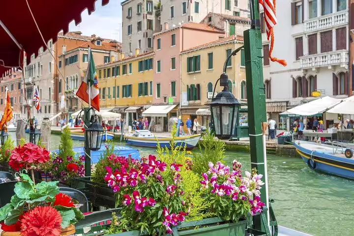 Colorful canal-side café with flowers and boats in Venice, perfect for a last minute private walking and boat tour