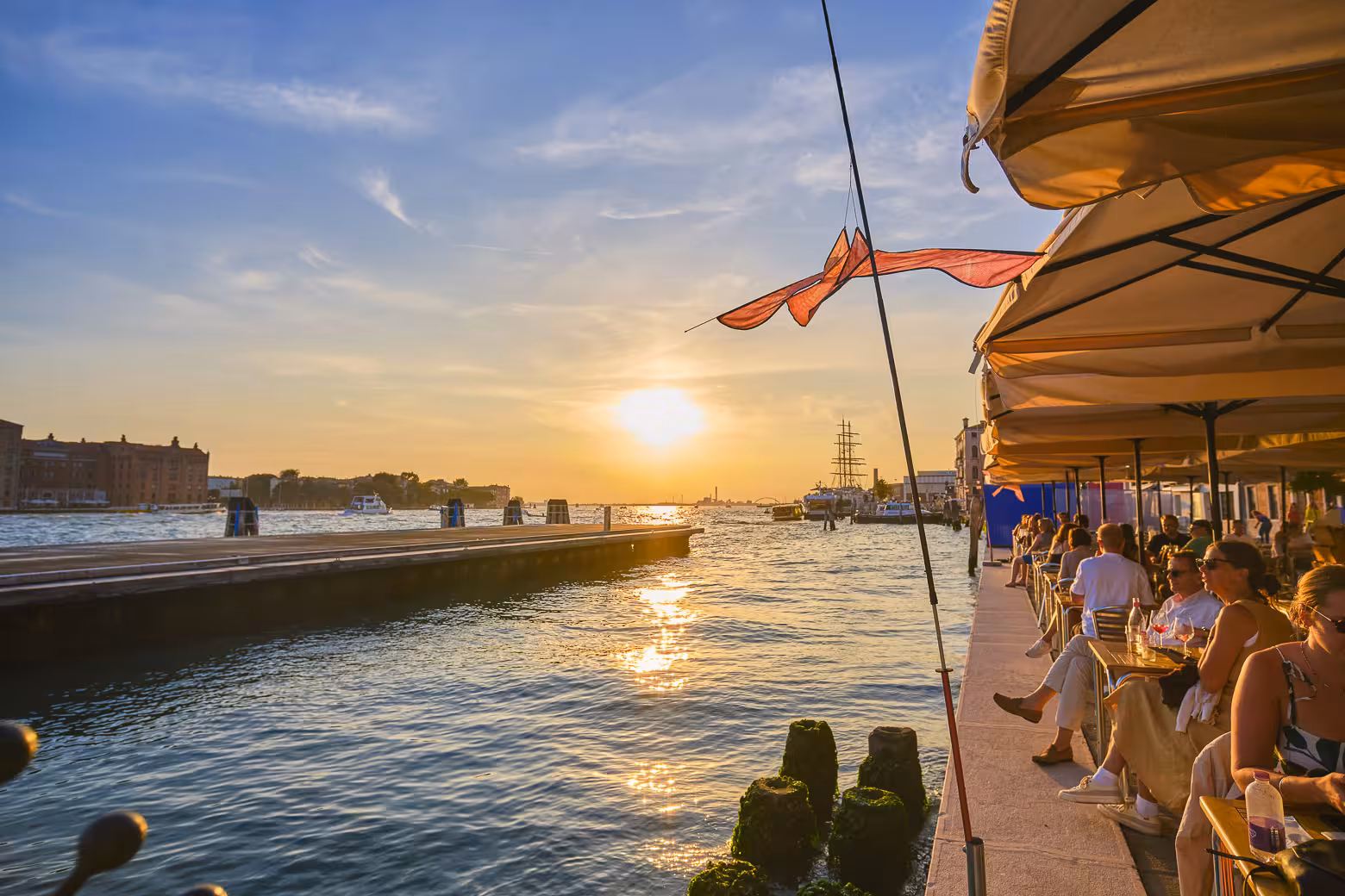 People enjoying sunset views from a bustling Venice canal-side café during a picturesque evening.