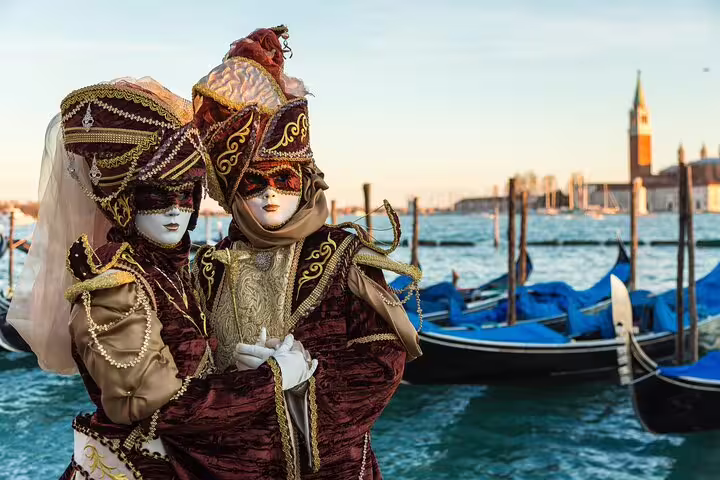 Venice Carnival masked couple in ornate costumes standing by moored gondolas, showcasing traditional Venetian culture