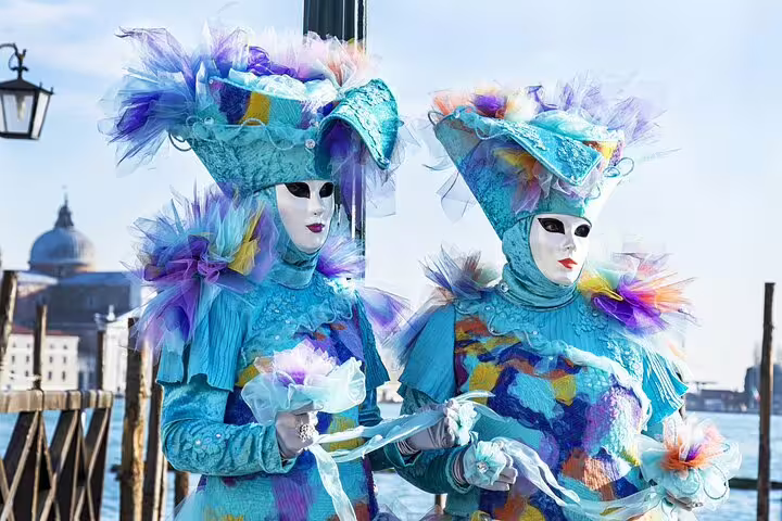 Costumed performers in vibrant Venetian carnival masks by the Grand Canal, enriching a guided Venice experience with St Mark’s Basilica