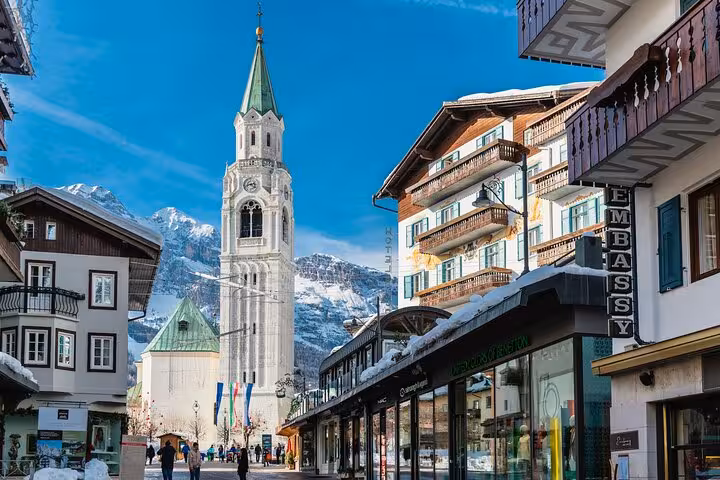 Scenic view of Cortina d'Ampezzo town center with bell tower and snow-capped mountains, perfect for travelers.