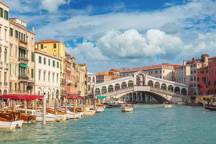 Classic view of Venice Grand Canal with gondolas, colorful palaces and the iconic Rialto Bridge under a bright blue sky