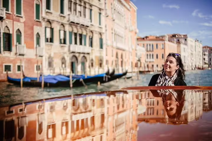 Woman enjoying a scenic gondola ride along Venice's historic canals with reflections of colorful buildings.
