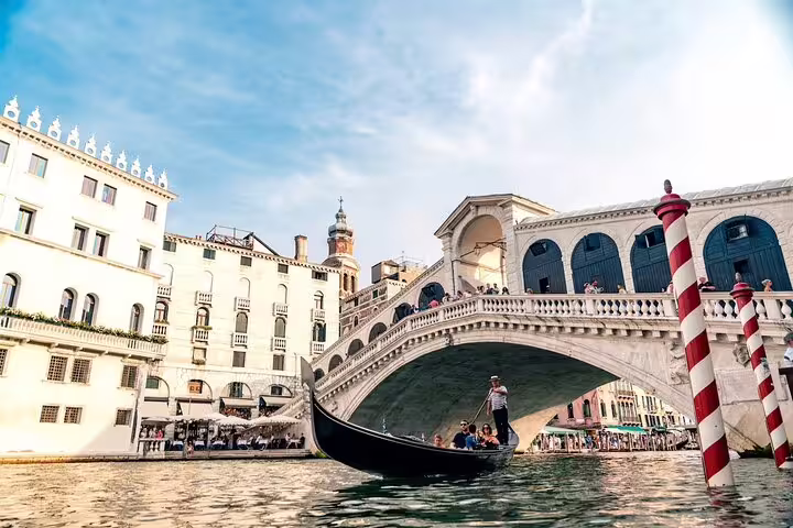 Traditional gondola with tourists gliding under the iconic Rialto Bridge on Venice Grand Canal during a private boat tour