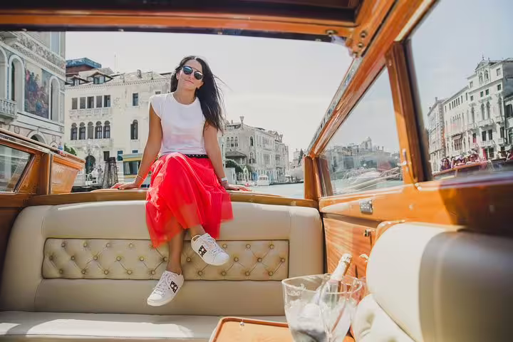 Woman enjoying a sunny boat ride on the Grand Canal in Venice, surrounded by historic buildings and vibrant scenery.