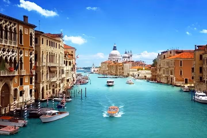 Experience Venice's vibrant Grand Canal with boats gliding past historic buildings under a bright blue sky.