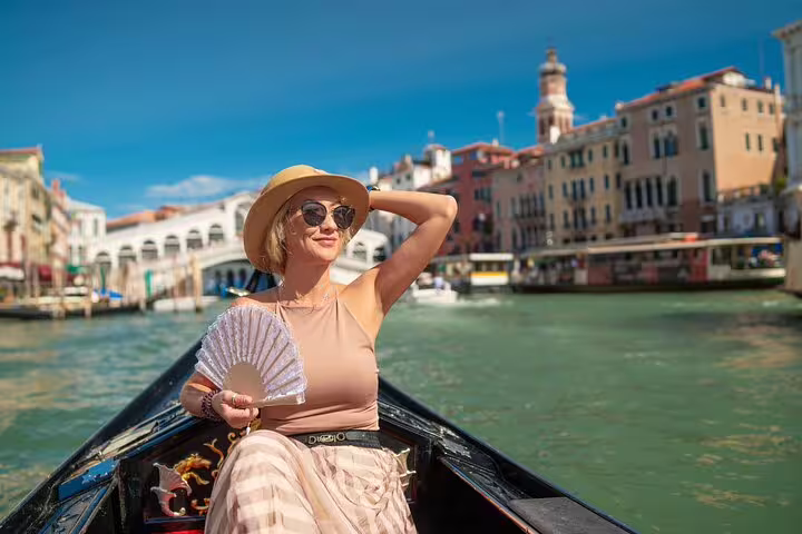 Woman relaxing on a private gondola ride along Venice Grand Canal with Rialto Bridge and historic palaces in the background