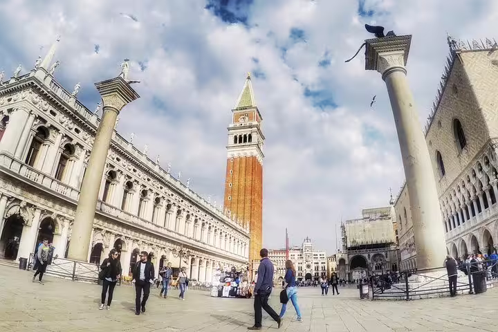 Tourists strolling through Venice's iconic St. Mark's Square with the towering Campanile and historic architecture around.