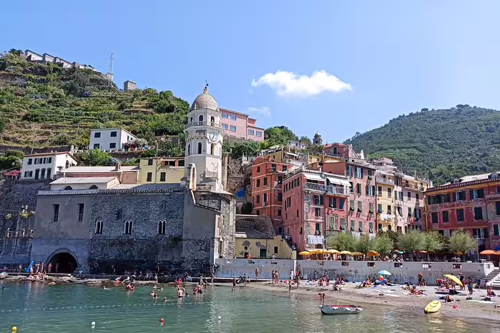 Vibrant Vernazza harbor in Cinque Terre with historic church, pastel houses and beachgoers on a sunny private day trip
